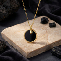 Gold snake pendant with green eyes and round black onyx on a stone slab lifestyle background.