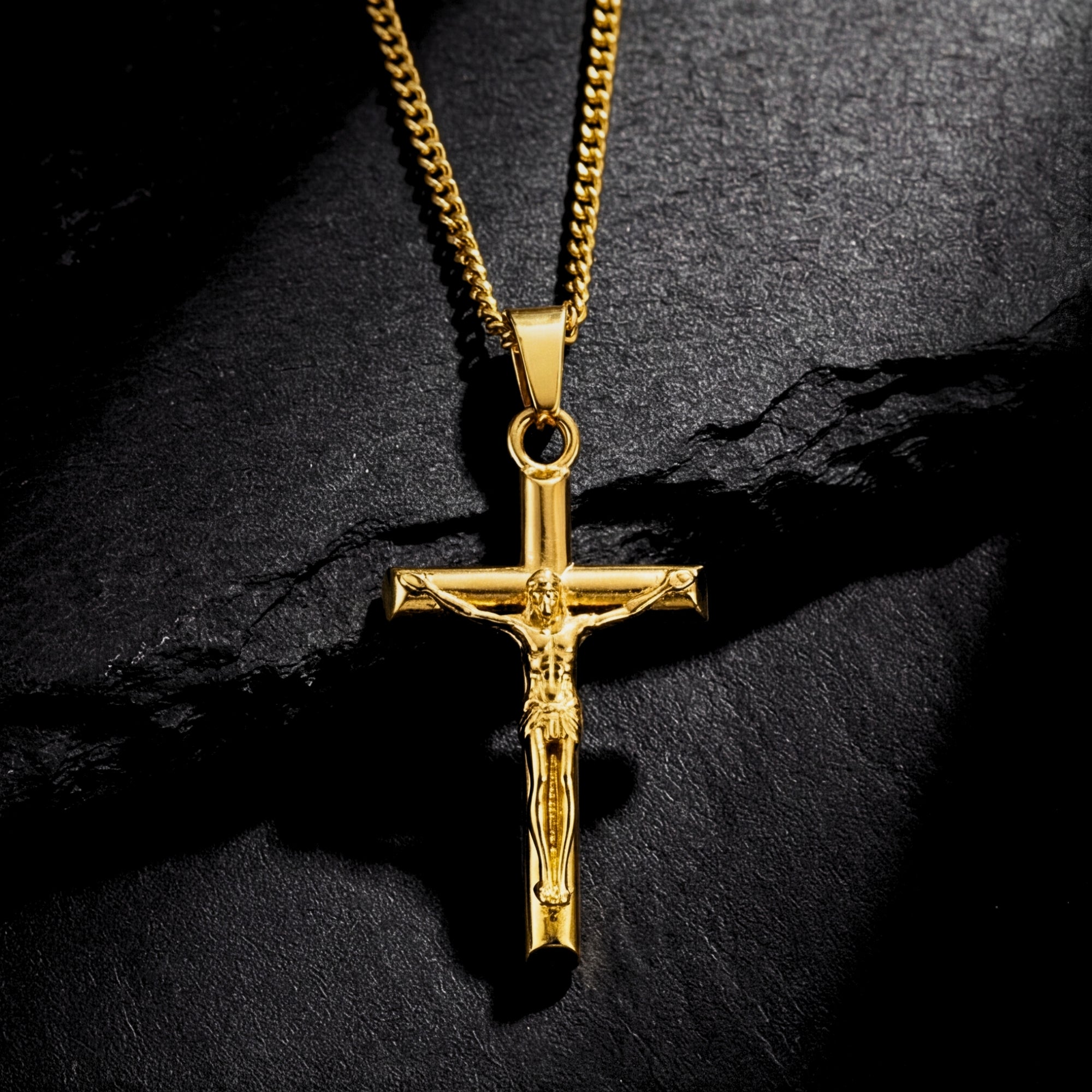 Gold stainless steel Divine Cross crucifix pendant on a curb chain, resting on a dark textured stone surface.