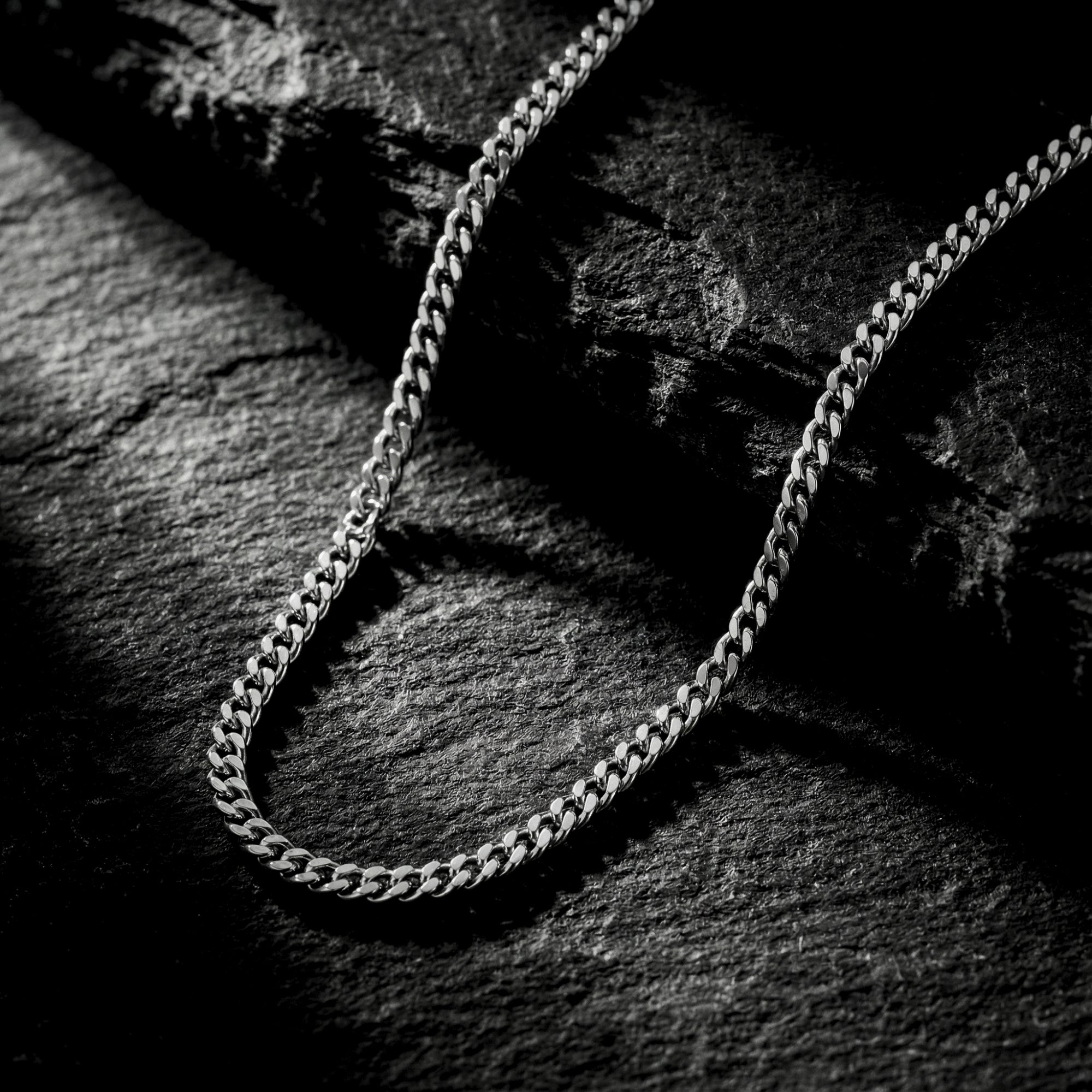 2mm silver stainless steel curb chain displayed on a dark, textured slate background.