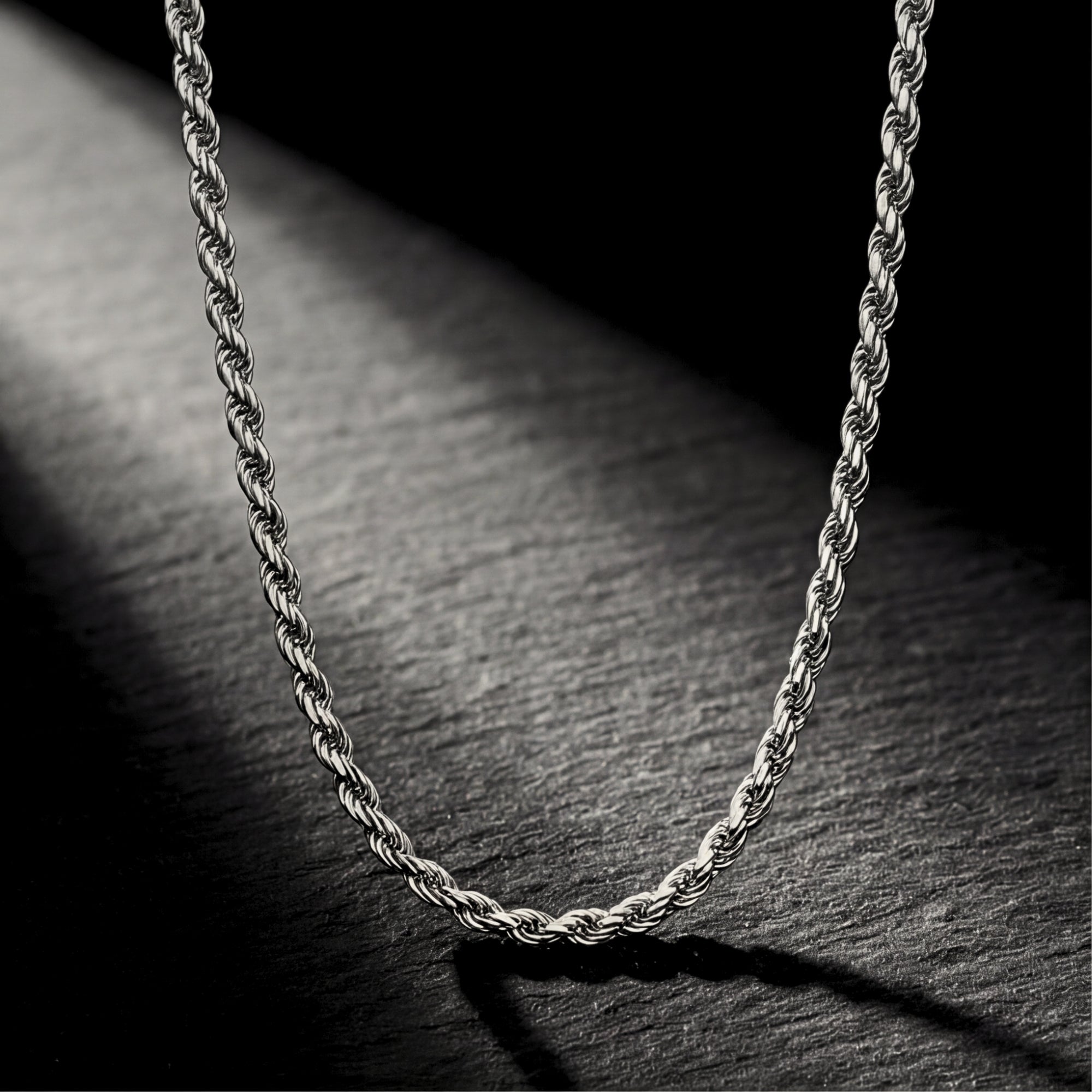 Silver stainless steel rope chain hanging against a dark textured stone background.