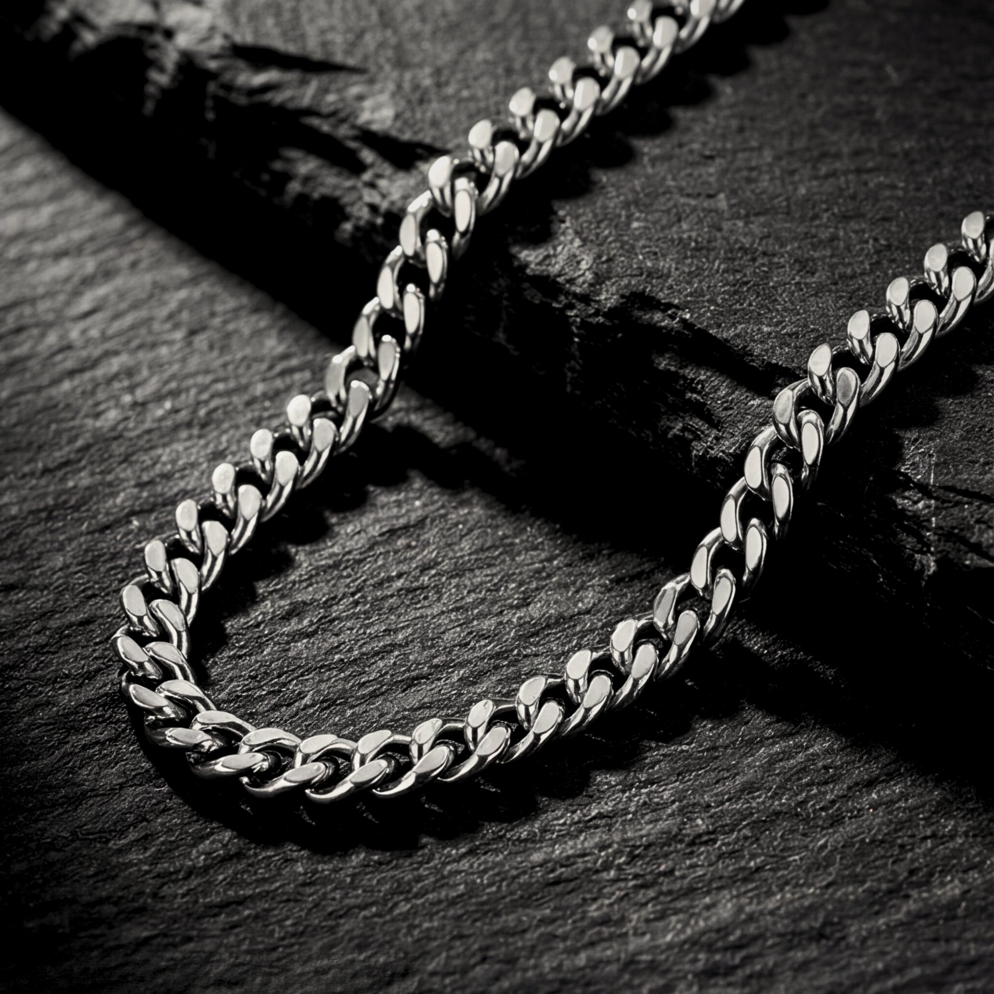 Close-up of silver 4mm stainless steel Cuban link chain links on a dark stone surface.