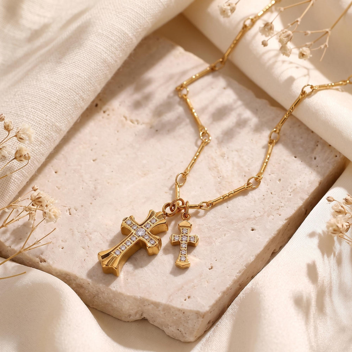 Gold-tone double cross pendant necklace with clear CZ stones, displayed on a pale stone slab.