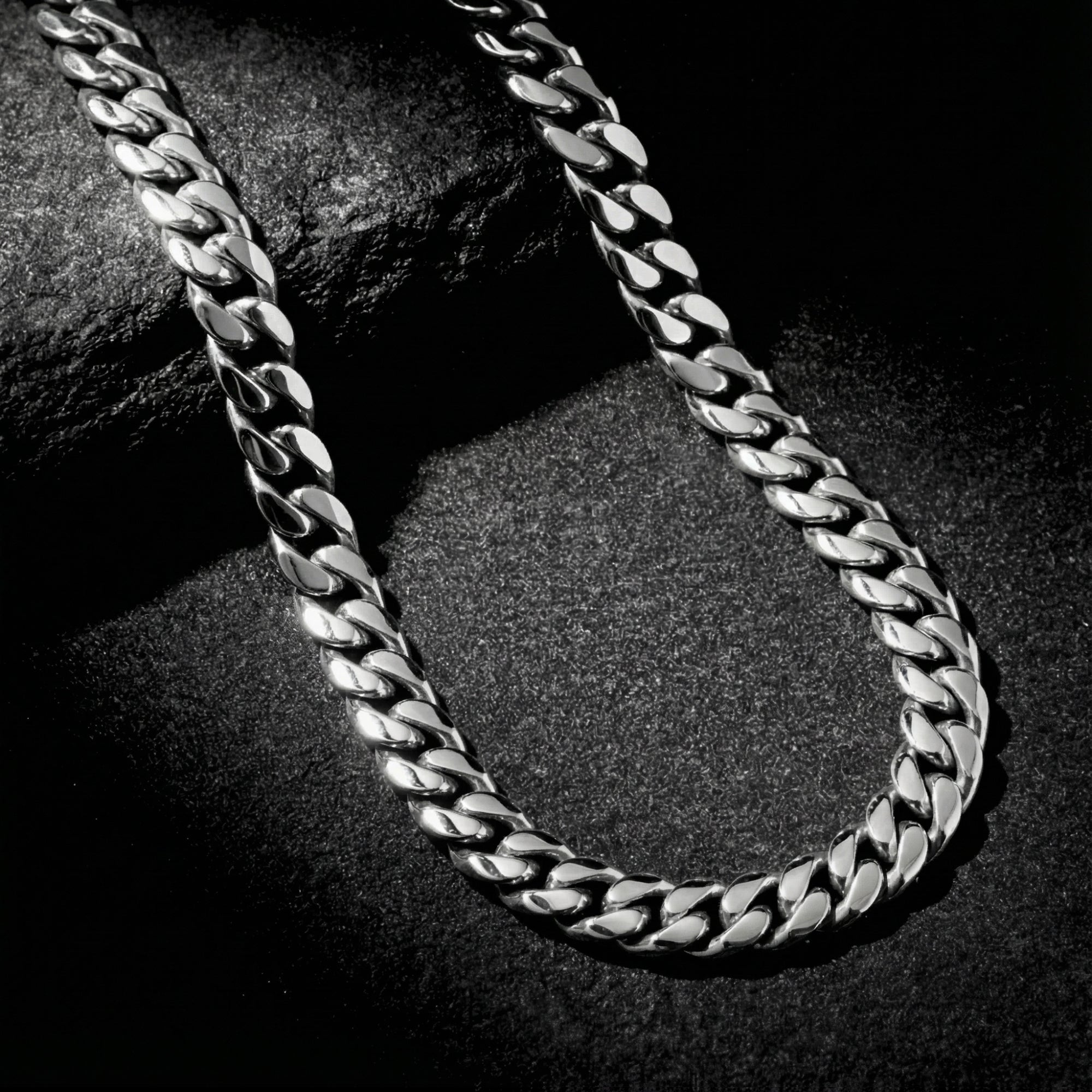 12mm silver stainless steel Cuban link chain necklace draped over a dark textured rock.