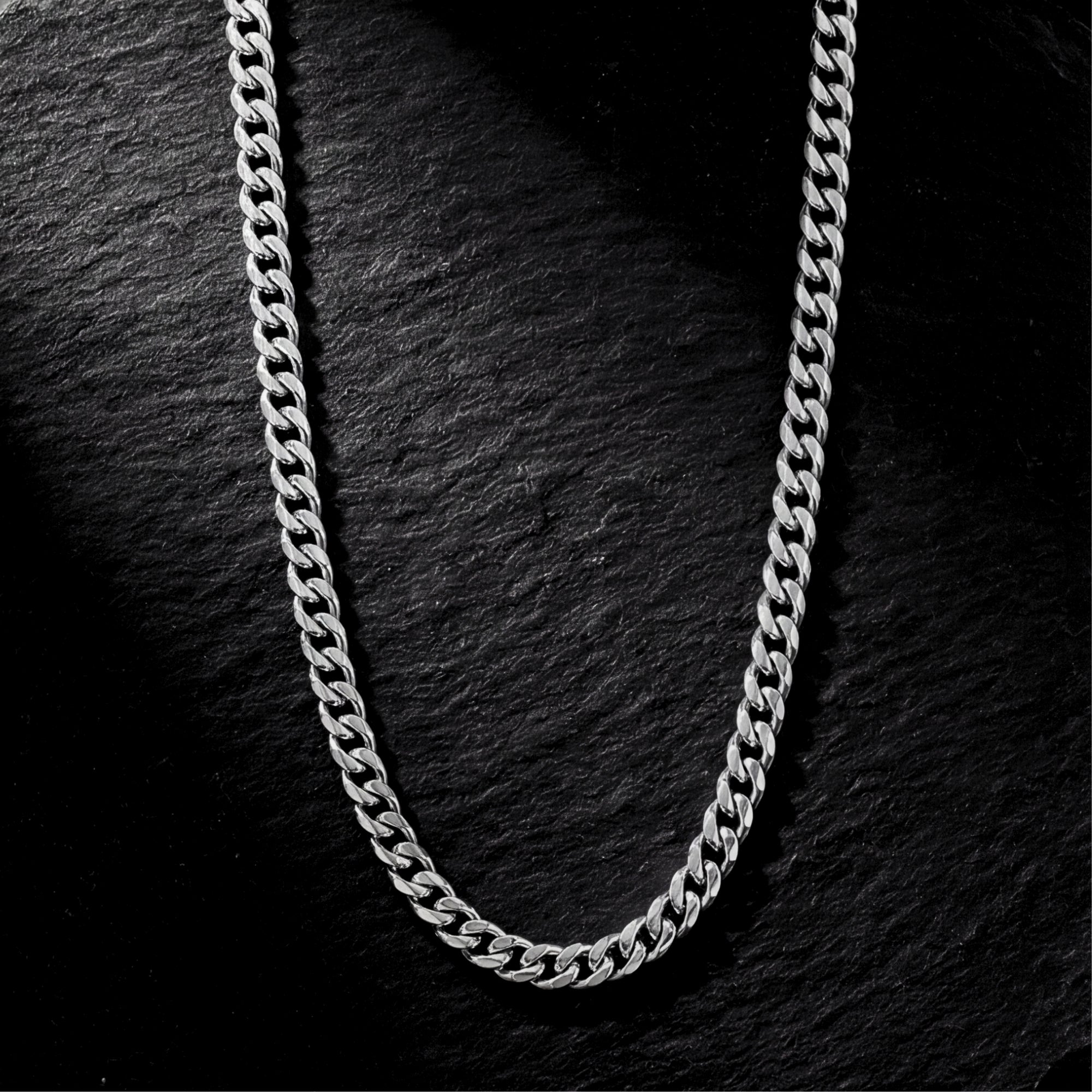 Silver 6mm stainless steel Cuban link chain laid flat on a dark textured slate background.