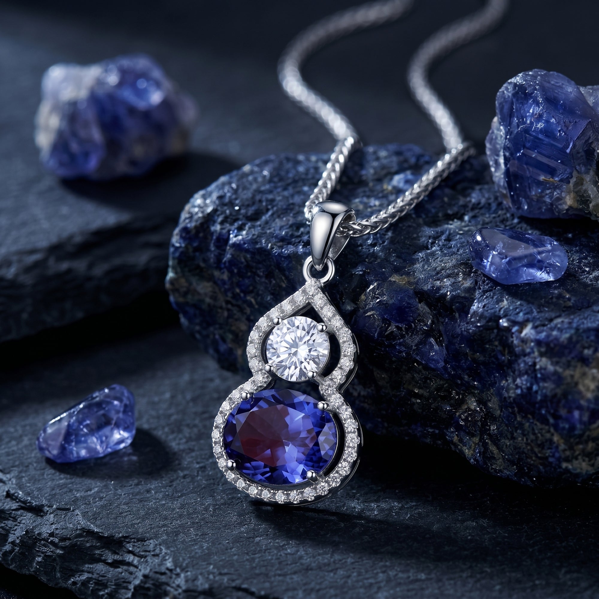 Oval tanzanite pendant necklace in white gold resting on raw blue gemstones in a lifestyle setting.