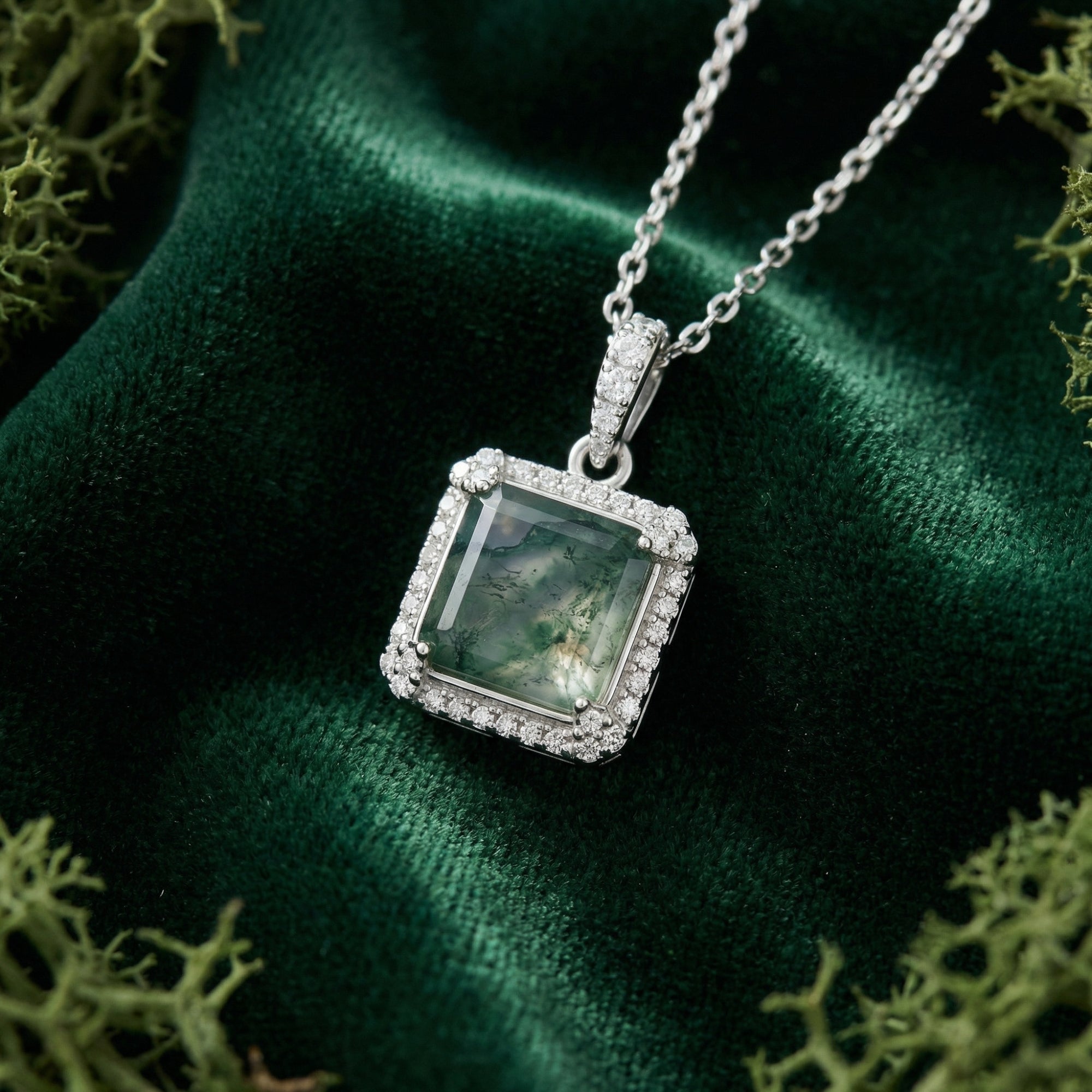 Square cut moss agate halo pendant necklace in sterling silver displayed on green velvet with natural moss.