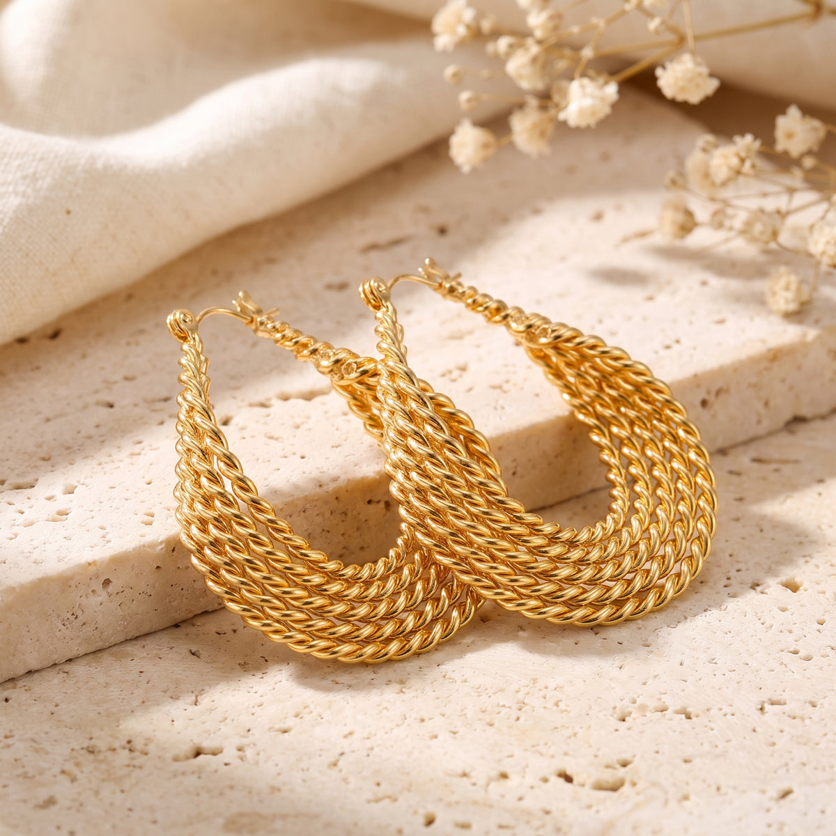 Pair of gold-tone multi-strand twisted rope drop earrings resting on a porous cream stone slab.