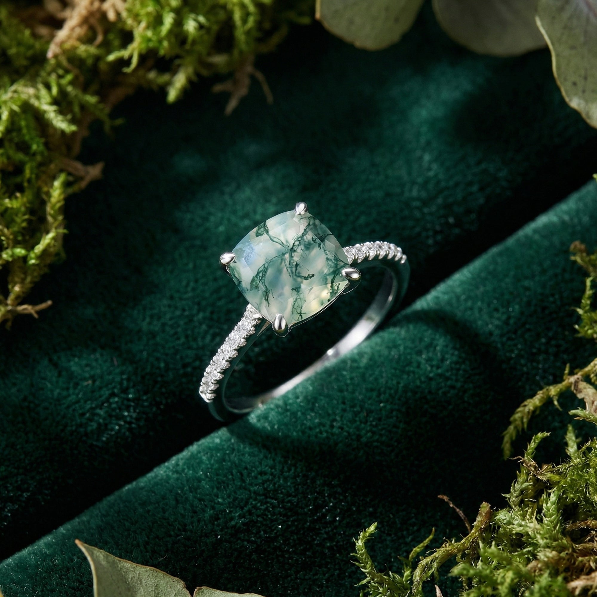 Cushion cut moss agate S925 sterling silver ring with a pavé band, displayed on green velvet with natural moss.