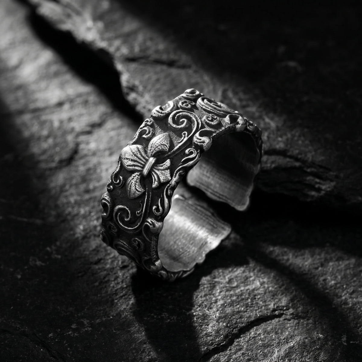 Angled close-up of the carved silver open-band ring with a fleur-de-lis motif on dark slate.