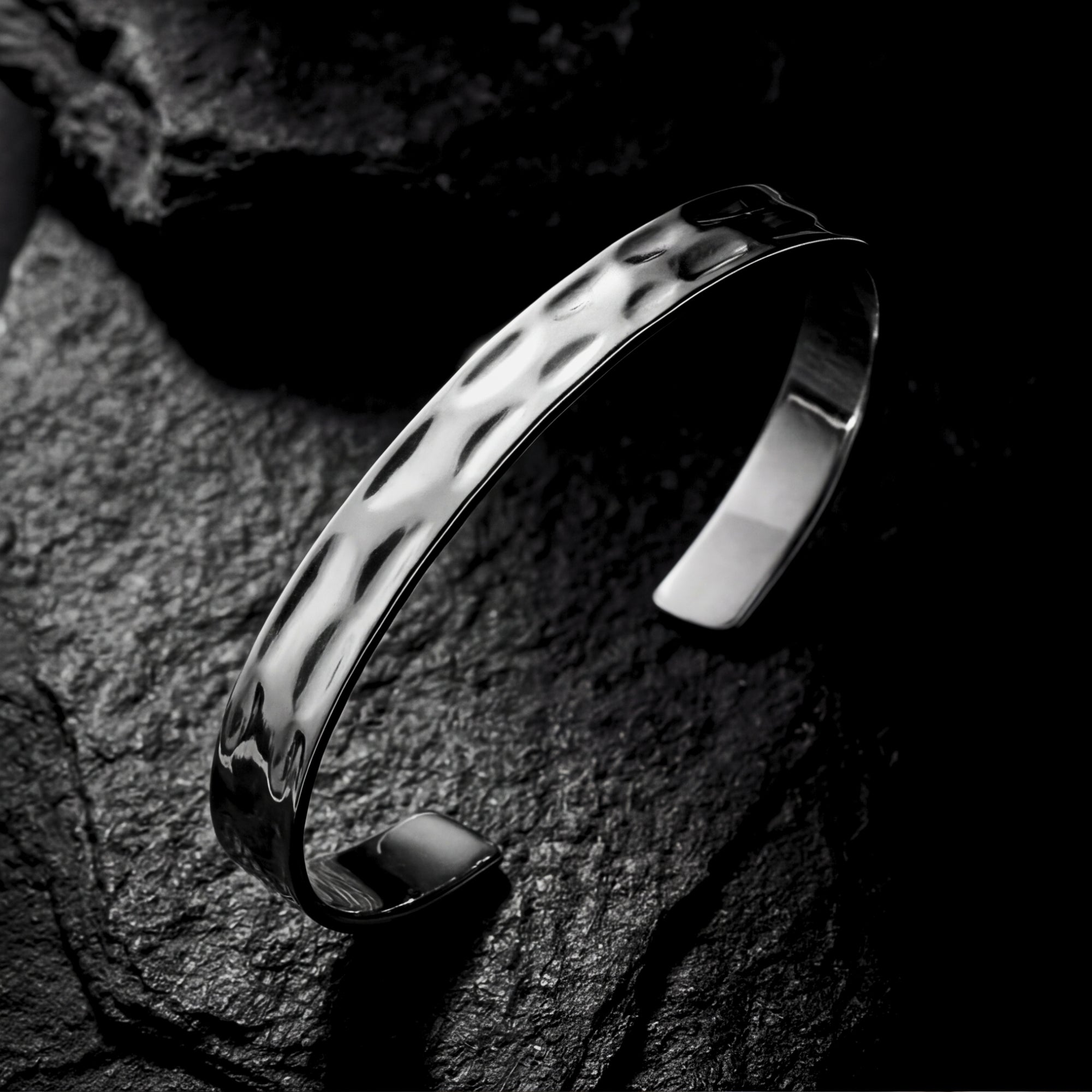 Silver hammered stainless steel cuff bangle shown at an angle on a dark, textured rock surface.