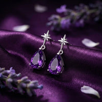 Pear cut amethyst drop earrings in sterling silver resting on purple silk with lavender sprigs.