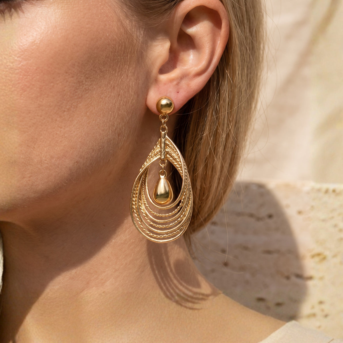 Close-up side view of one gold-toned layered teardrop earring worn on an earlobe.