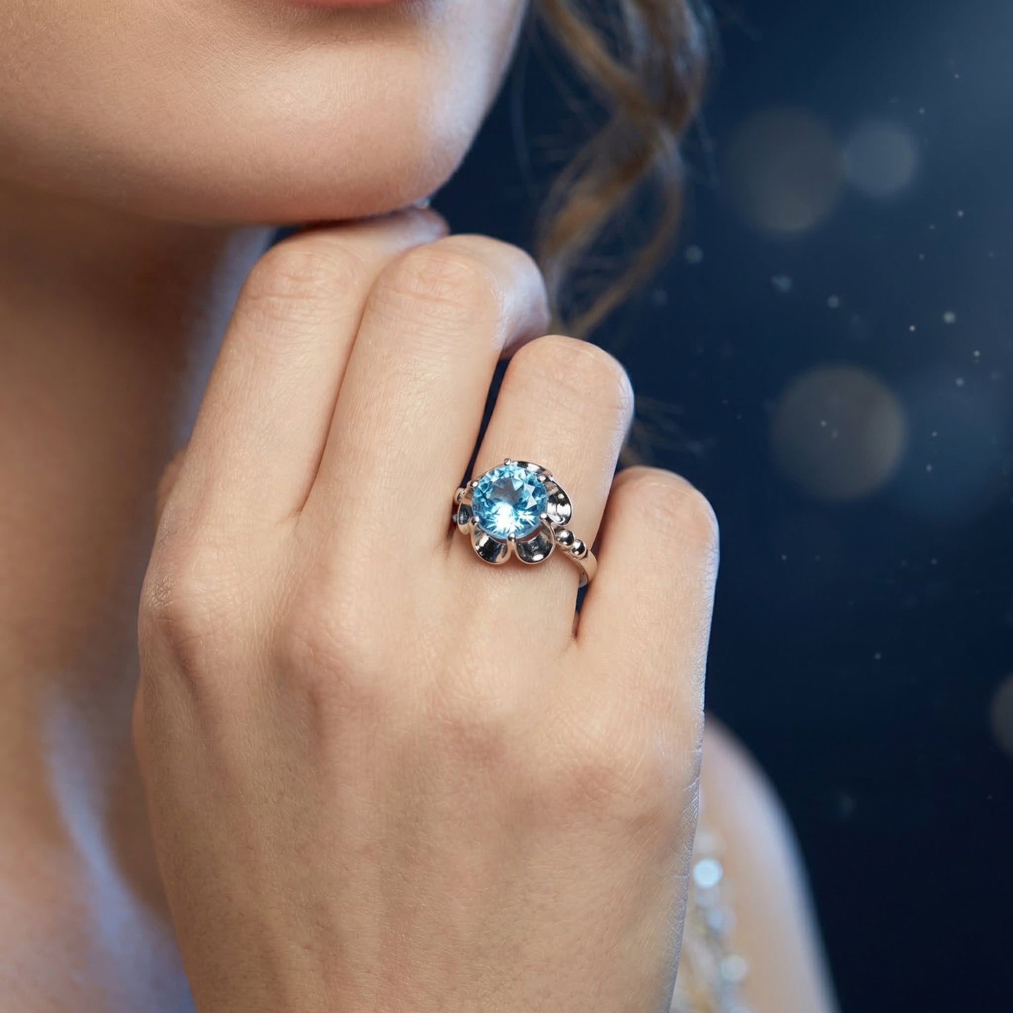 Sterling silver ring with a round blue topaz worn on a woman's hand against a dark bokeh background.