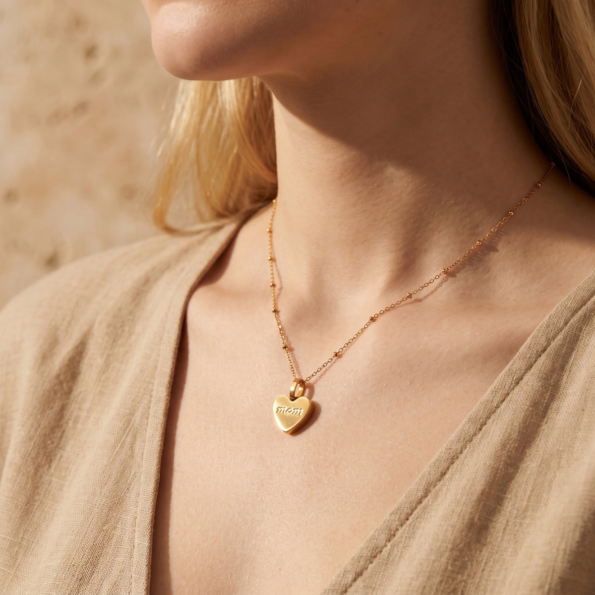 Model wearing the gold-tone heart pendant engraved with 'mom', shown resting on the neck.