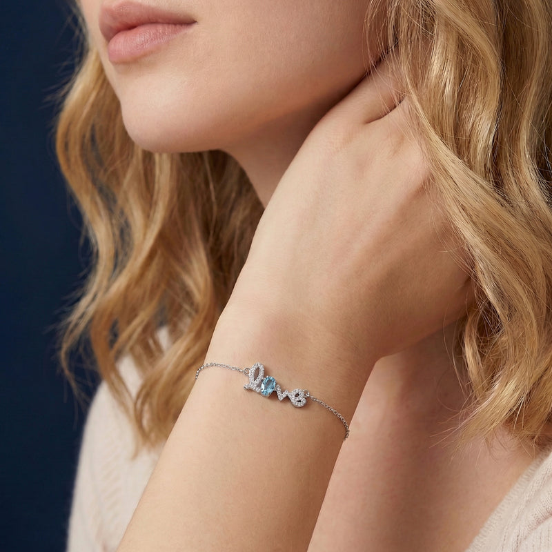 Woman wearing the silver Swiss Blue Topaz Love bracelet with an oval cut gemstone on her wrist.