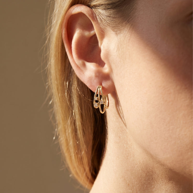 Gold moissanite triple hoop earrings worn on a woman's ear.