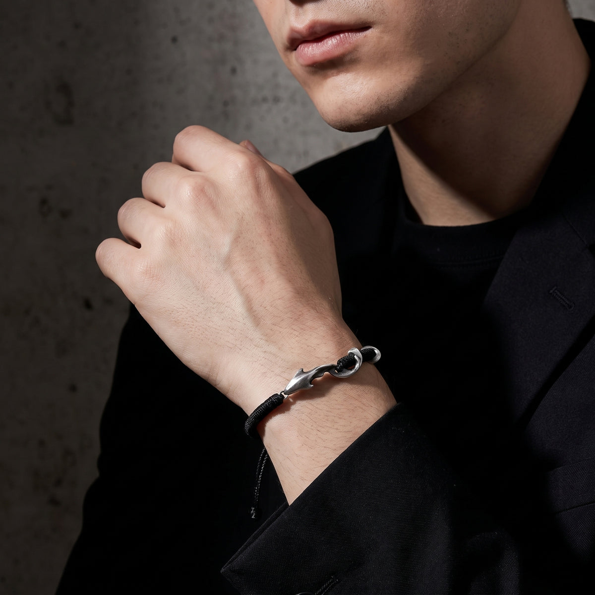 Model wearing the black cord dolphin hook bracelet on his wrist with a dark blazer.