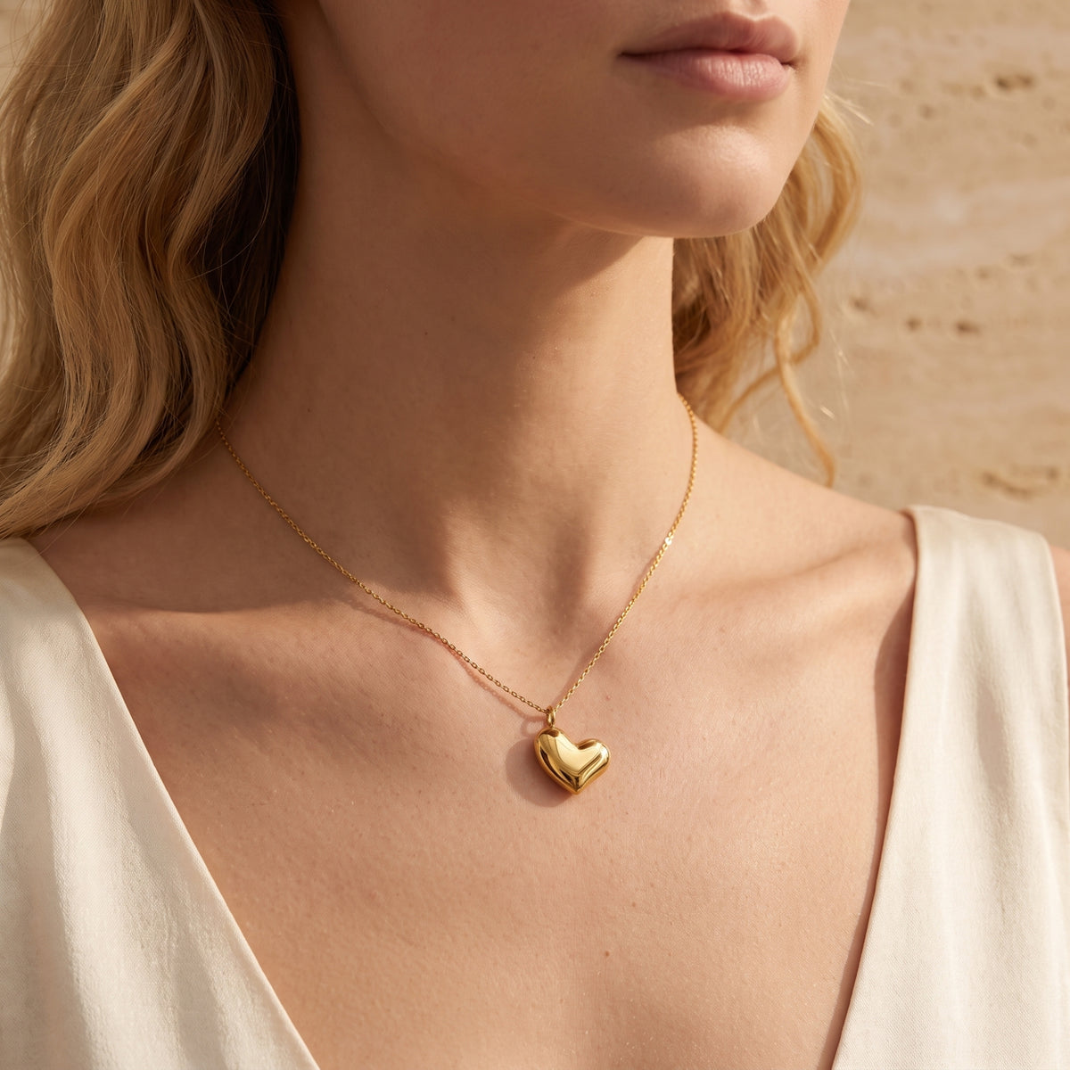 Front view of a woman wearing the gold-tone puffed heart necklace with a white V-neck top.