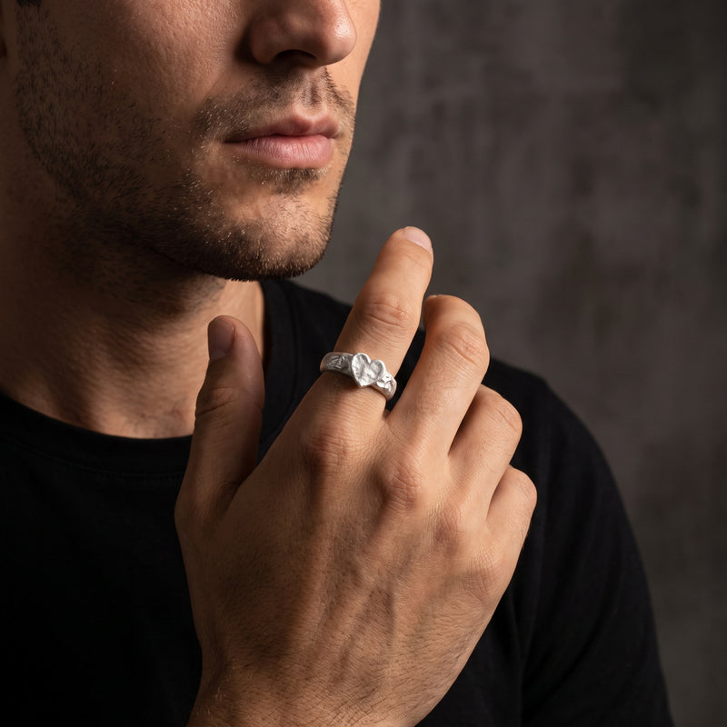 Man wearing the hammered heart ring on his index finger with his hand raised near his face.