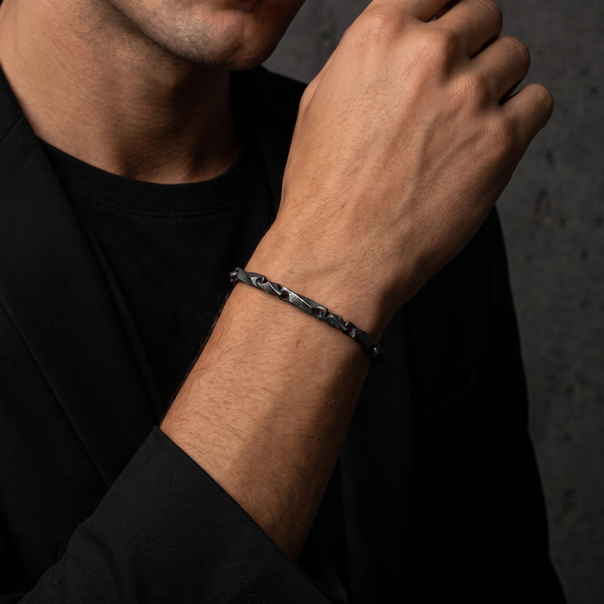 Dark oxidized silver twisted-link bracelet worn on a man's wrist over a black blazer.