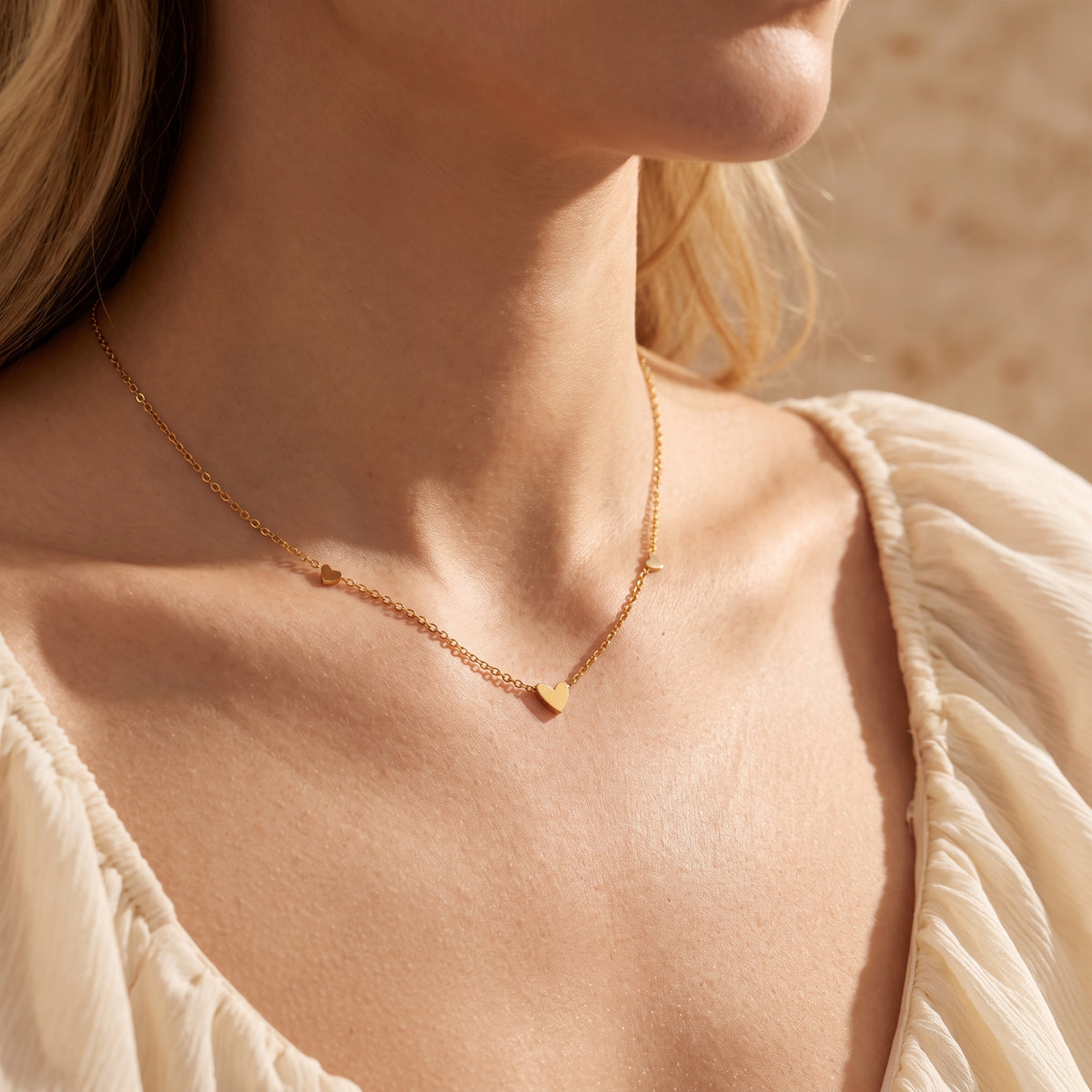 Model wearing the gold-tone heart station necklace resting along her collarbone with a cream blouse.