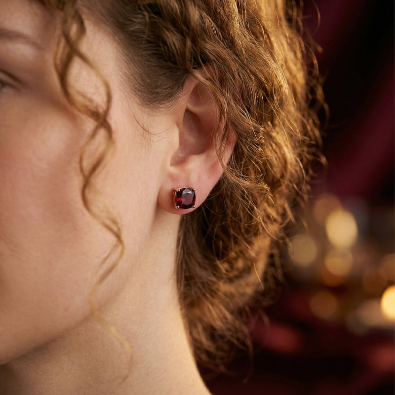 Cushion cut red garnet stud earring in 18K rose gold shown on a model's ear.