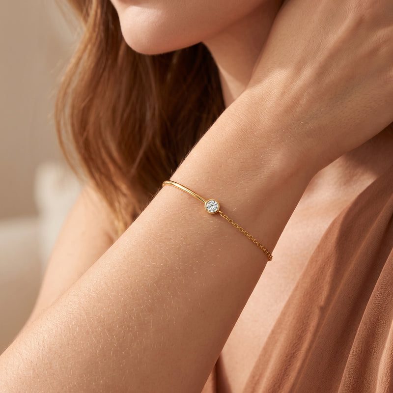 Close-up of a model wearing the gold-tone bezel station cuff bracelet with a round clear stone on her wrist.