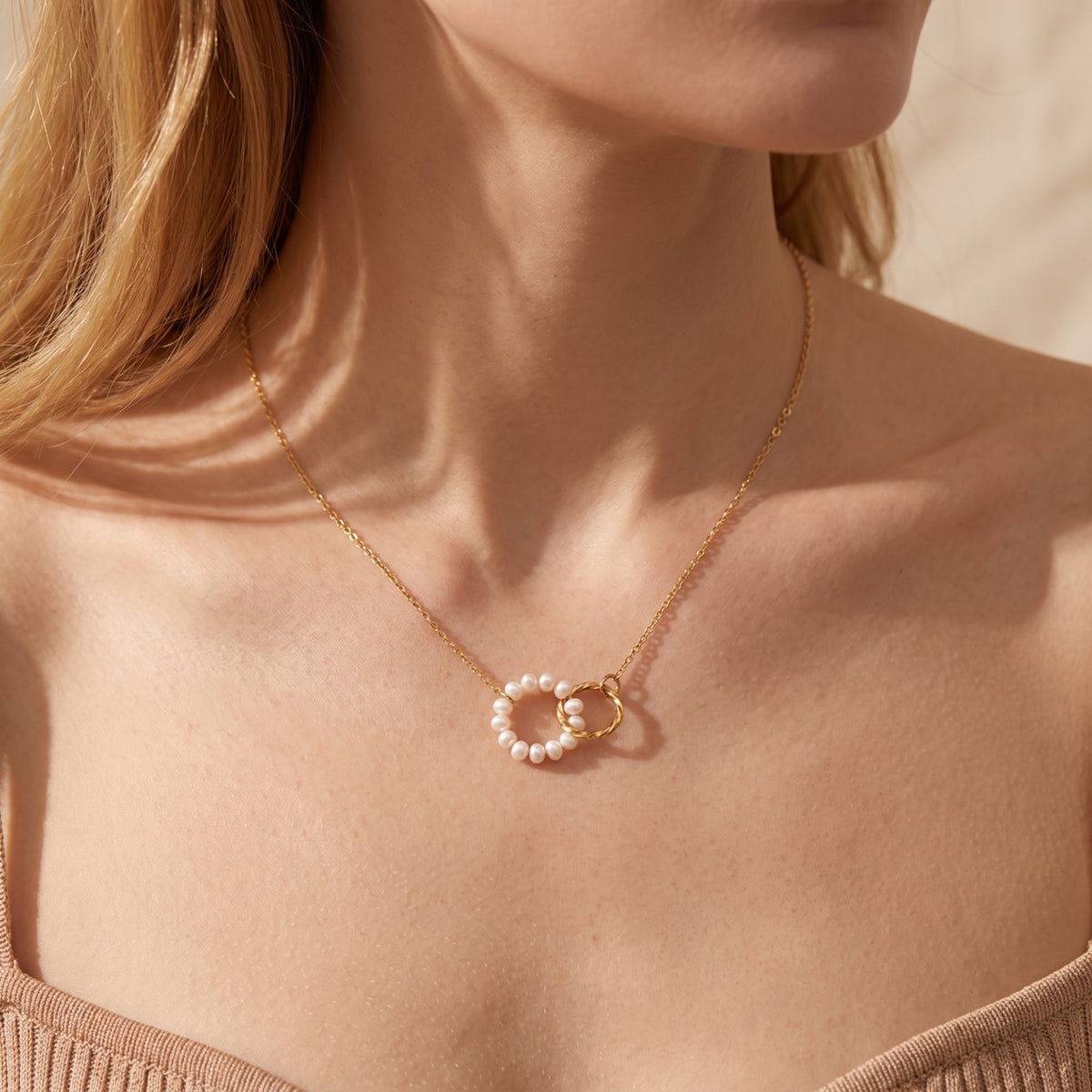 Close-up of a model wearing the gold-tone necklace with a pearl circle and twisted interlocking ring pendant.