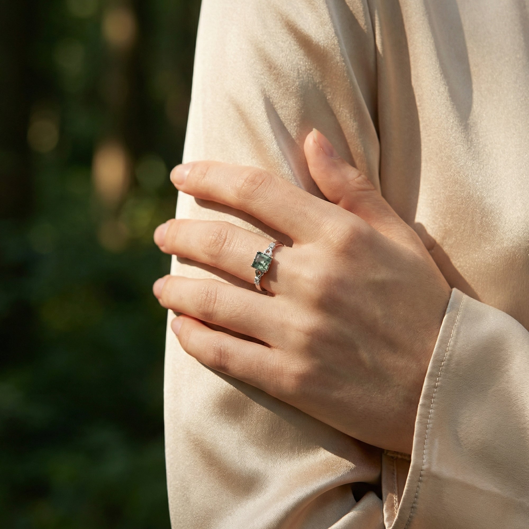 Model wearing the cushion cut natural moss agate silver ring on her finger against a soft outdoor background.