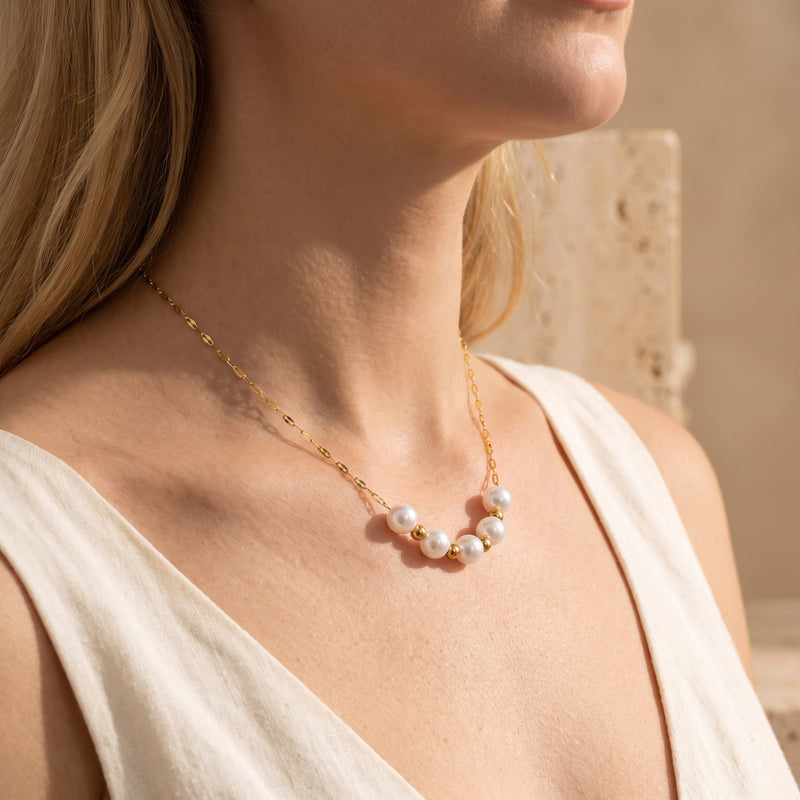 Side view of a model wearing the gold-tone station necklace with alternating white pearls and small gold-tone beads.