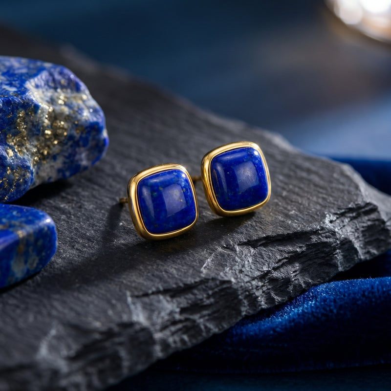Macro view of cushion cut natural lapis lazuli earrings in yellow gold settings on a textured rock background.