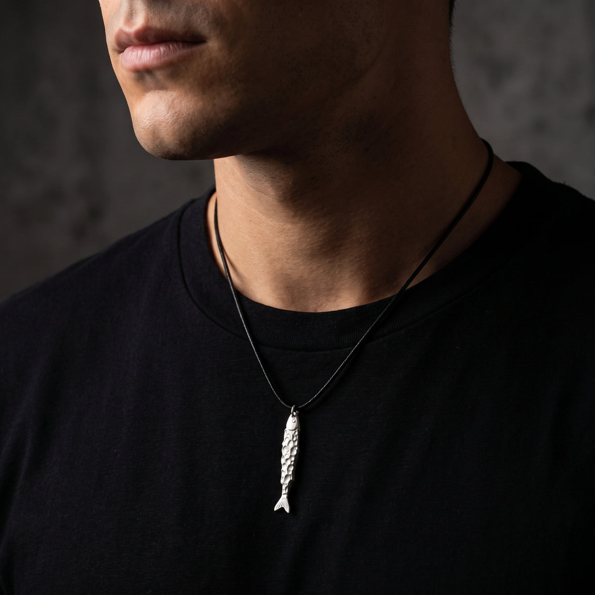 Front view of a man wearing the textured silver fish pendant necklace over a black crewneck shirt.