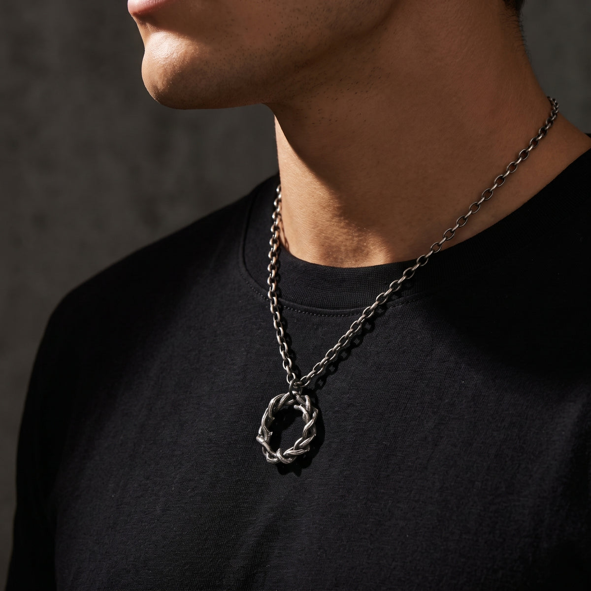 Side-profile view of a man wearing the silver intertwined circle pendant over a black shirt.
