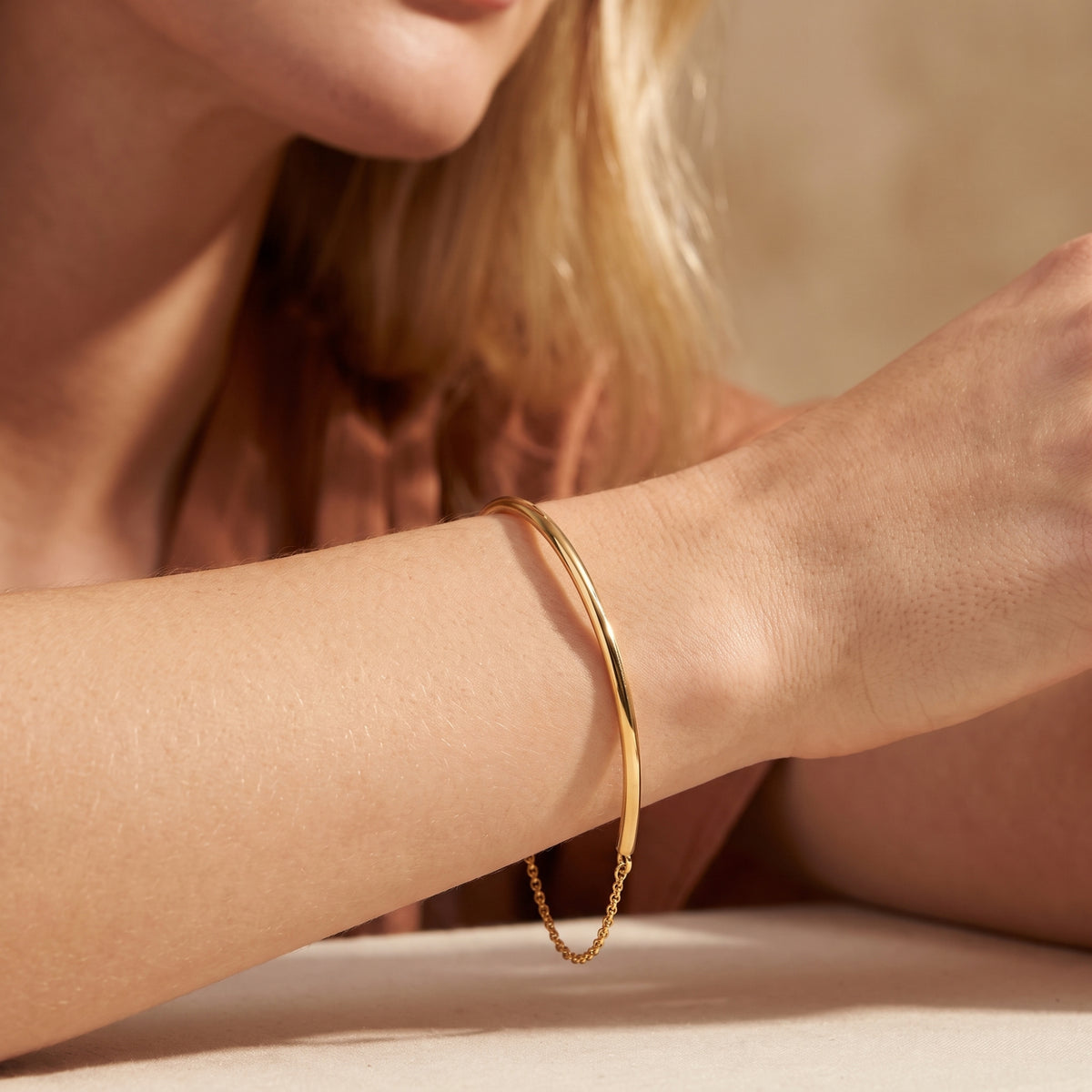 Gold-toned half-bangle bracelet worn on a wrist, with its chain hanging below.