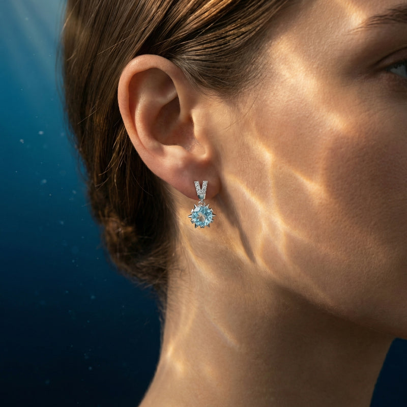 Woman wearing a round cut aquamarine drop earring in platinum with a diamond-accented V-shaped post.