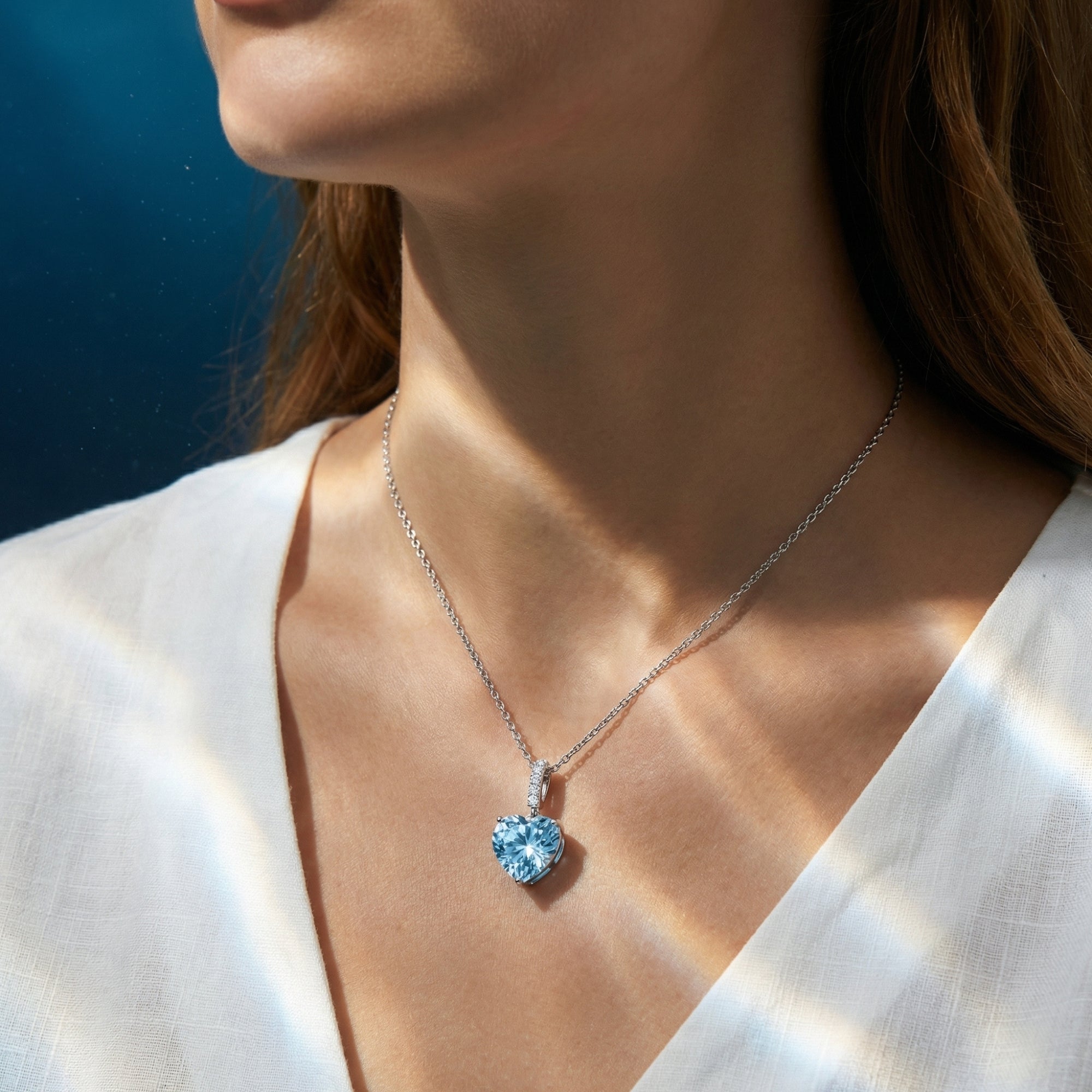 Woman wearing the heart cut aquamarine pendant necklace in platinum over a white V-neck shirt.