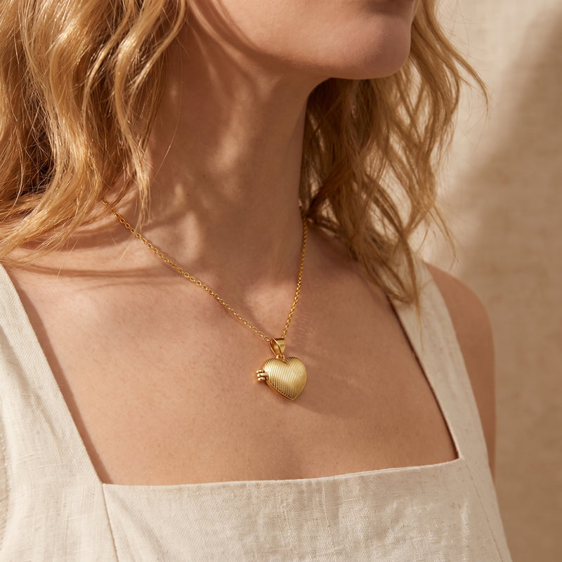 Gold-tone ribbed heart locket necklace worn on a model's chest with a square-neck top.
