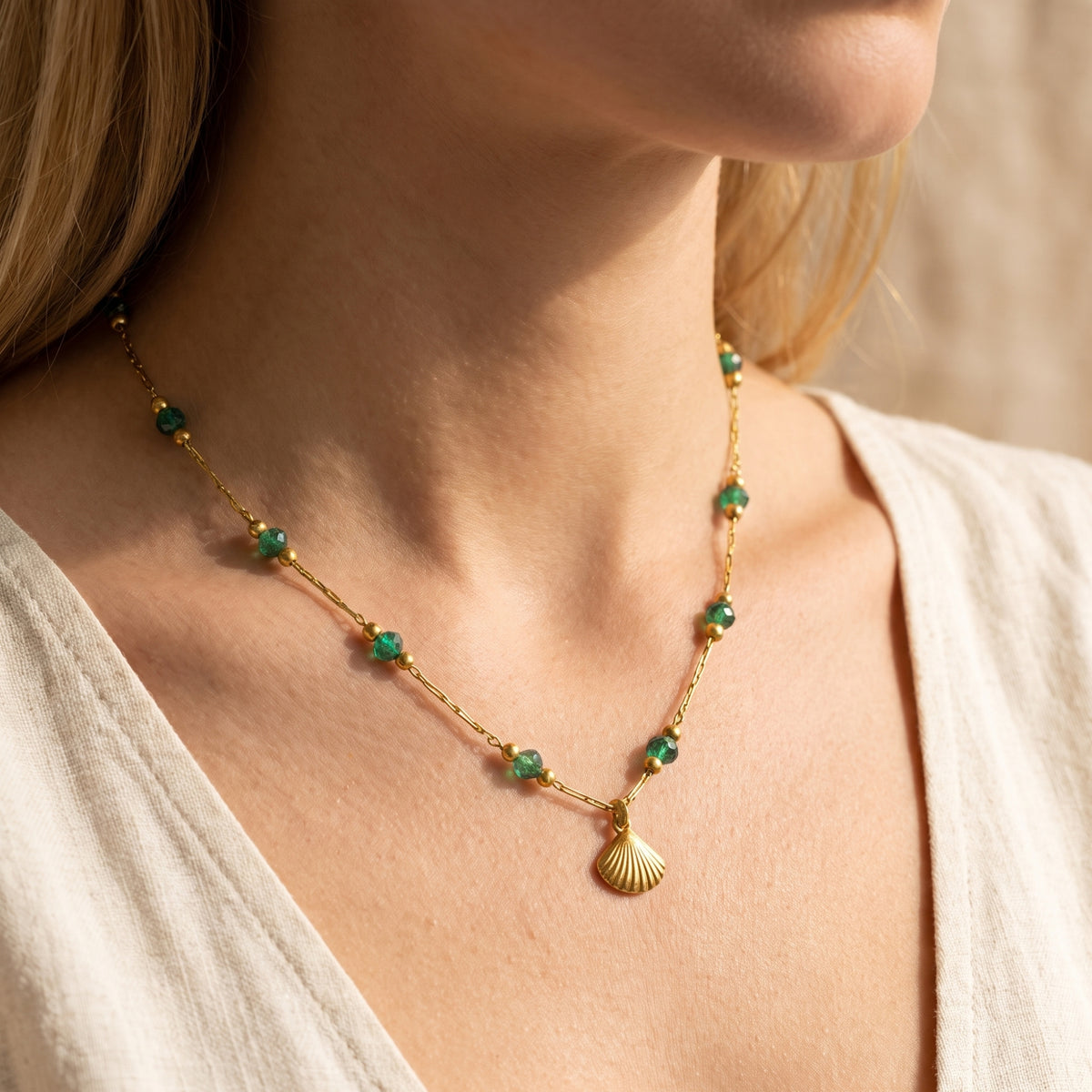 Side-angle view of a model wearing the gold-tone necklace with green beads and a shell pendant.