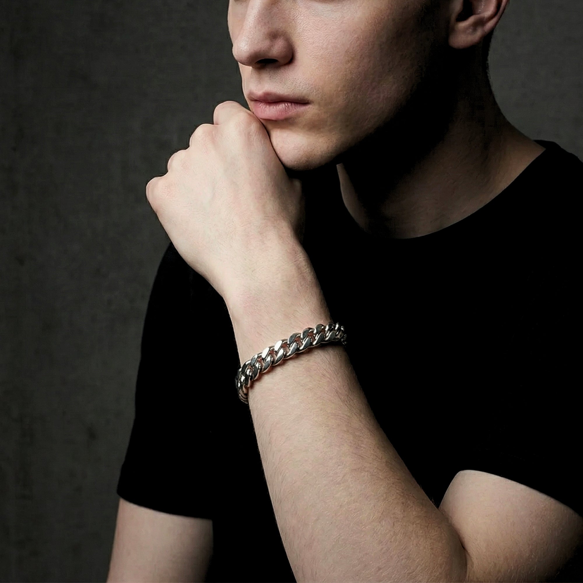 Silver 12mm stainless steel Cuban link bracelet worn on a man's wrist against a dark background.