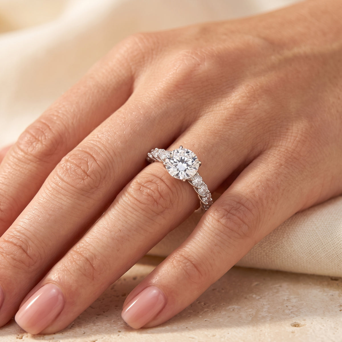 Silver round-cut solitaire ring with accent stones shown worn on a finger in a close-up hand view.