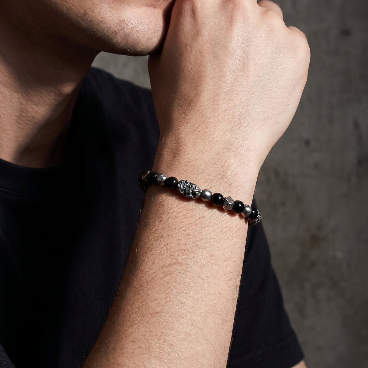 Close-up of a man wearing the black and silver beaded bracelet on his wrist with his hand raised.
