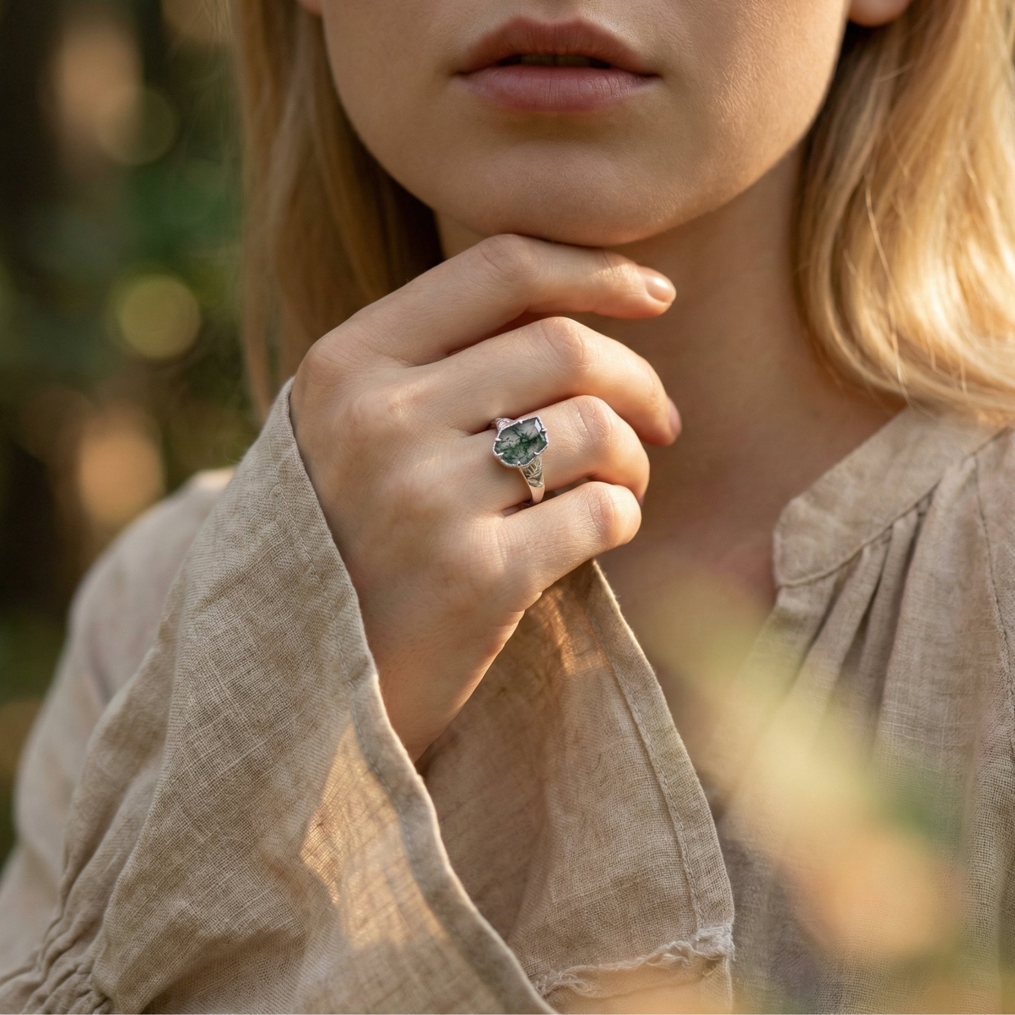 Woman wearing the sterling silver moss agate leaf ring on her finger in a natural outdoor setting.