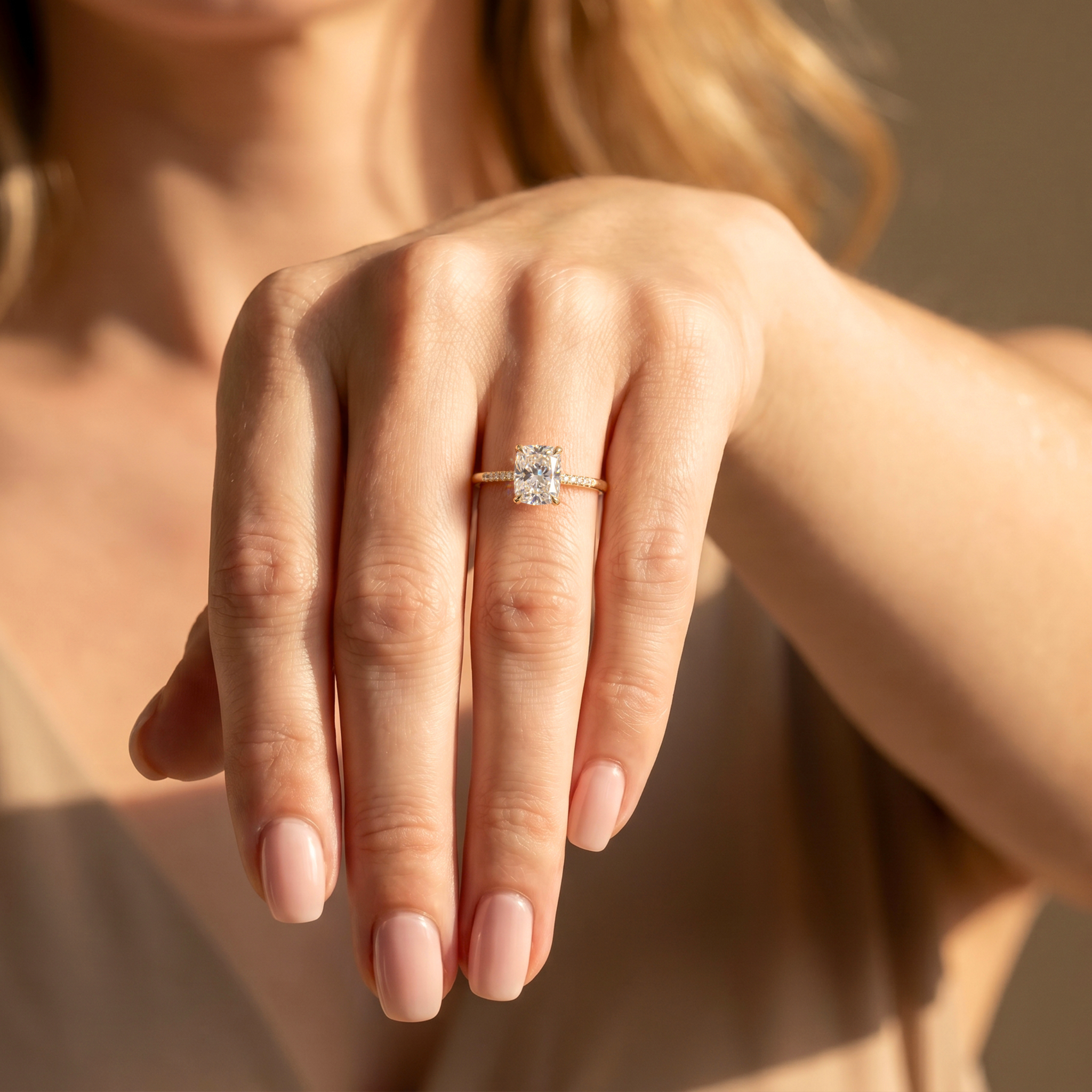 A woman wearing a yellow gold cushion cut moissanite engagement ring with a pavé diamond band on her ring finger.