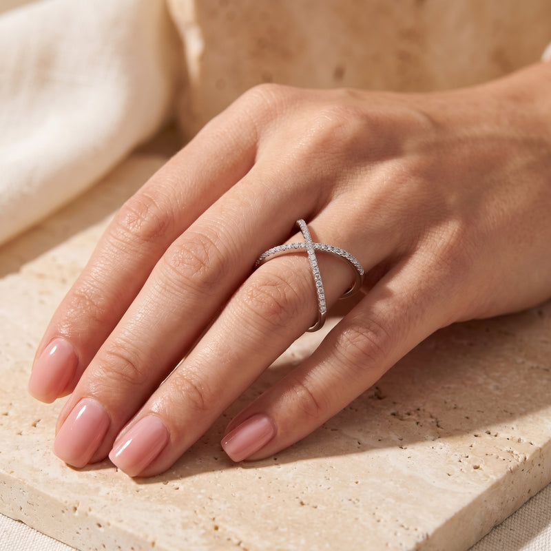 Hand wearing the silver criss-cross ring set with pavé stones, resting on a beige stone surface.