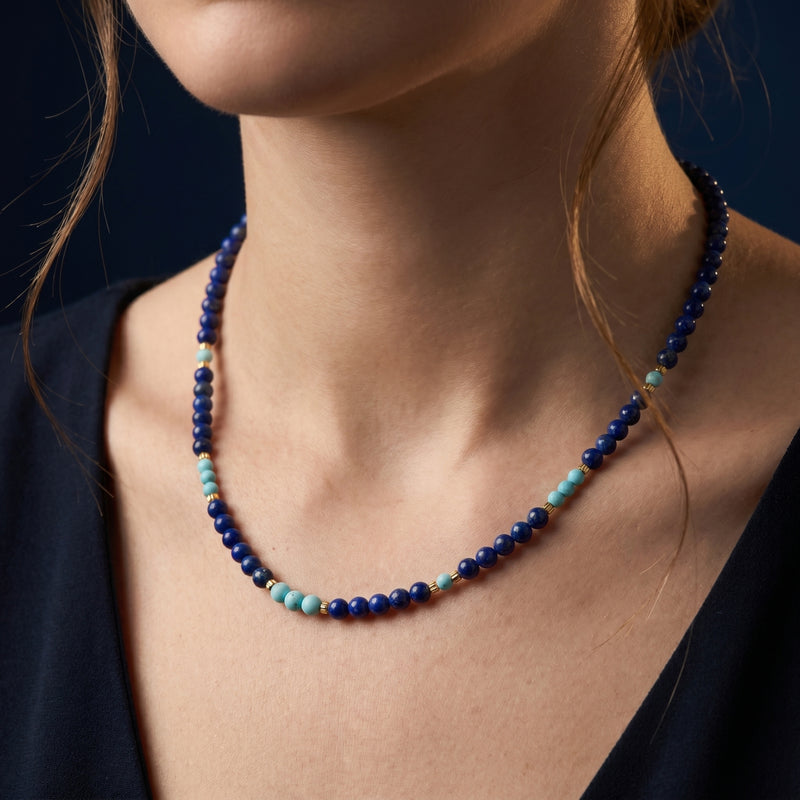 Woman wearing the Astral Path lapis lazuli necklace with light blue accents and gold beads.