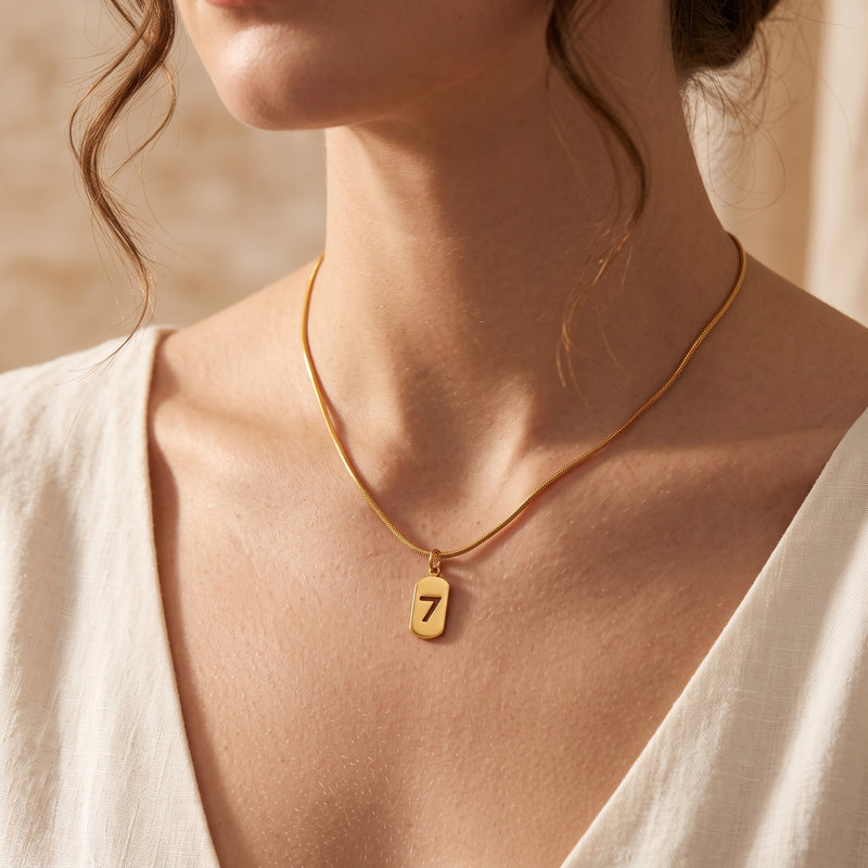 Model wearing the gold-tone cutout number 7 pendant necklace on a snake chain with a V-neck white top.