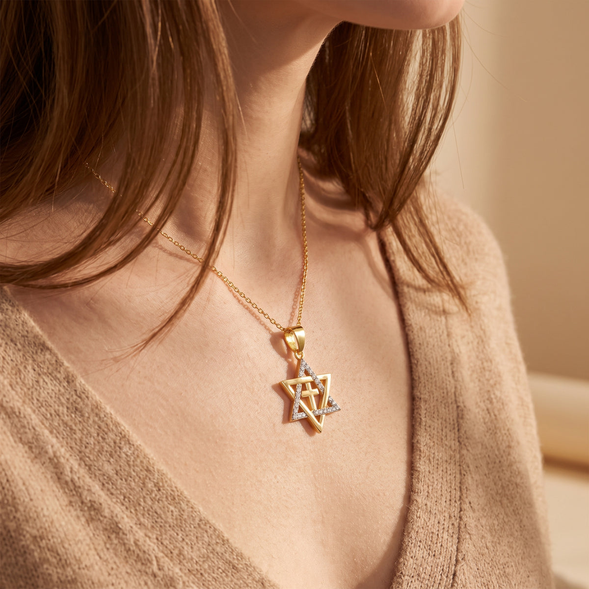 Model wearing a gold-tone Star of David cross pendant necklace over a beige knit cardigan.