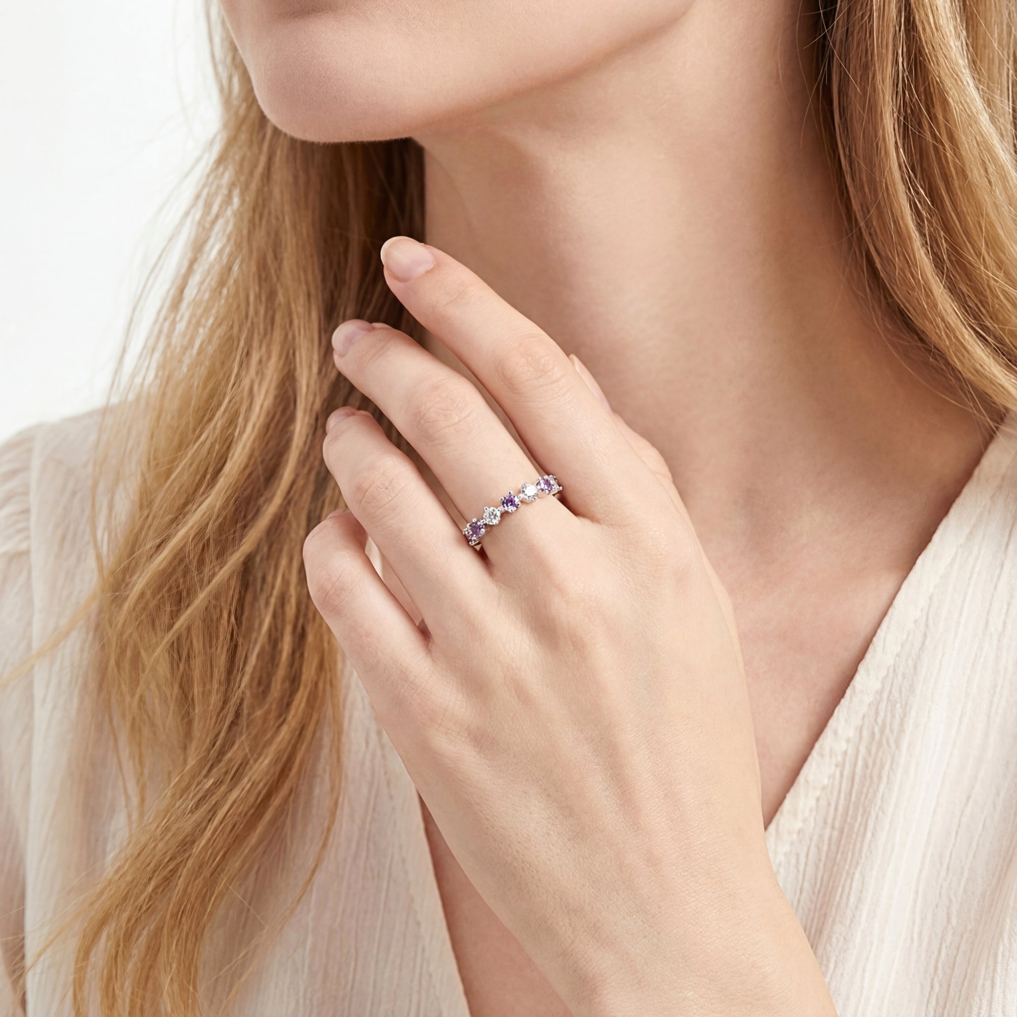 Woman wearing the sterling silver amethyst eternity band on her ring finger, paired with a cream blouse.