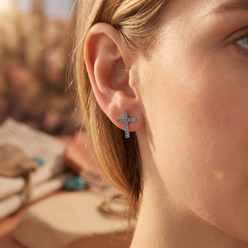Woman wearing a sterling silver cross earring set with vibrant blue turquoise stones on her earlobe.