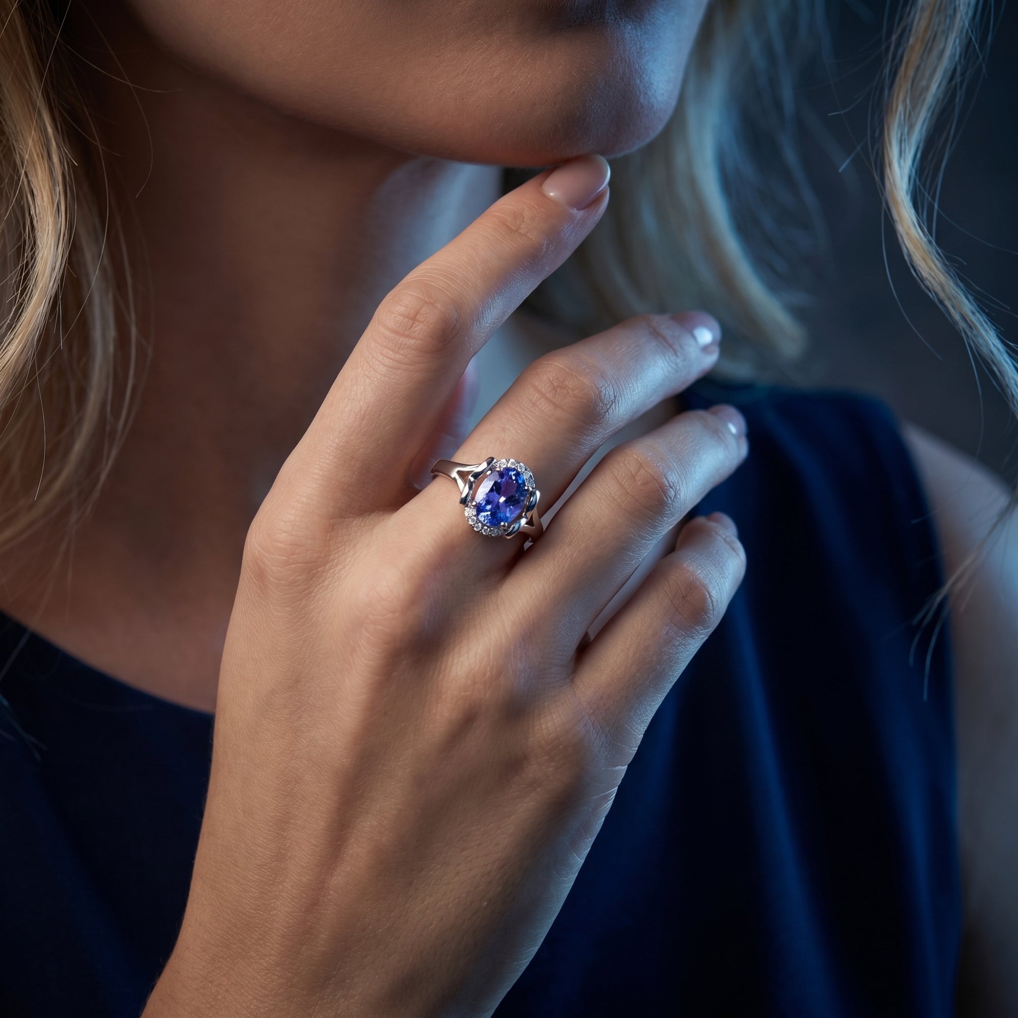Close-up of a woman wearing the 18K white gold oval tanzanite and diamond halo ring on her hand.